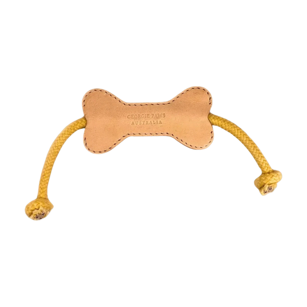 A Georgie Paws Flora Bone Dog Toy featuring a tan leather bone shape with yellow braided rope handles at each end. The toy is designed for durability, ideal for power chewers, and showcases the brand name embossed on the leather.